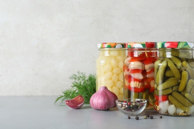 Photo of Glass jars with pickled vegetables on grey table against light background. Space for text