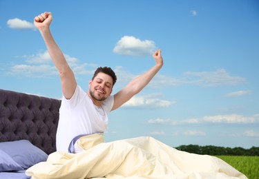 Image of Happy man stretching in bed and beautiful view of green field on background. Sleep well - stay healthy