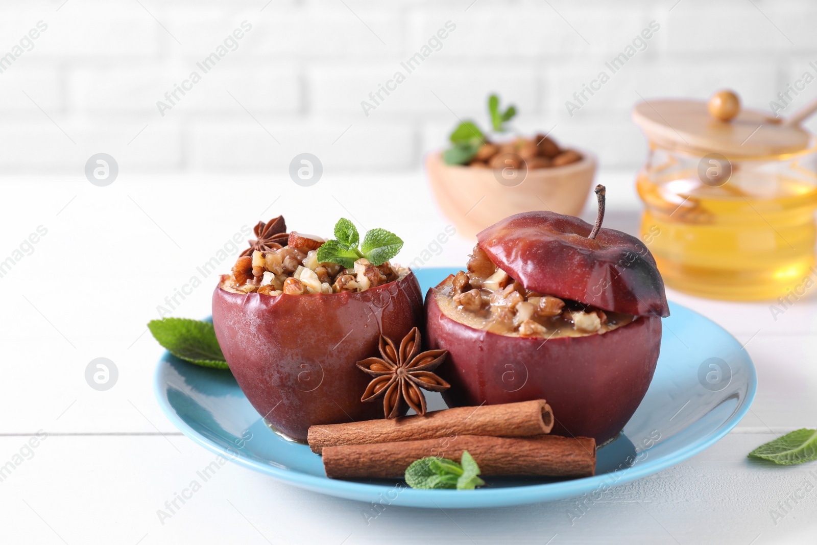 Photo of Tasty baked apples with nuts, honey, spices and mint on white wooden table