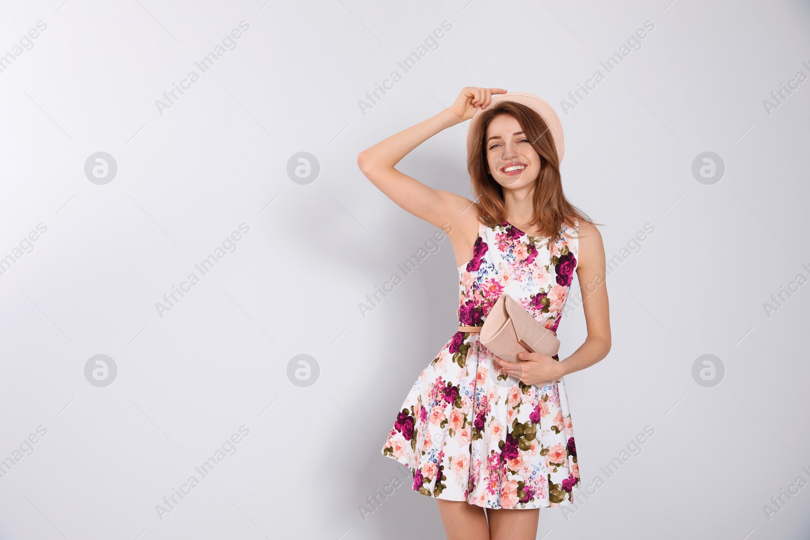 Photo of Young woman wearing floral print dress with clutch on light background. Space for text