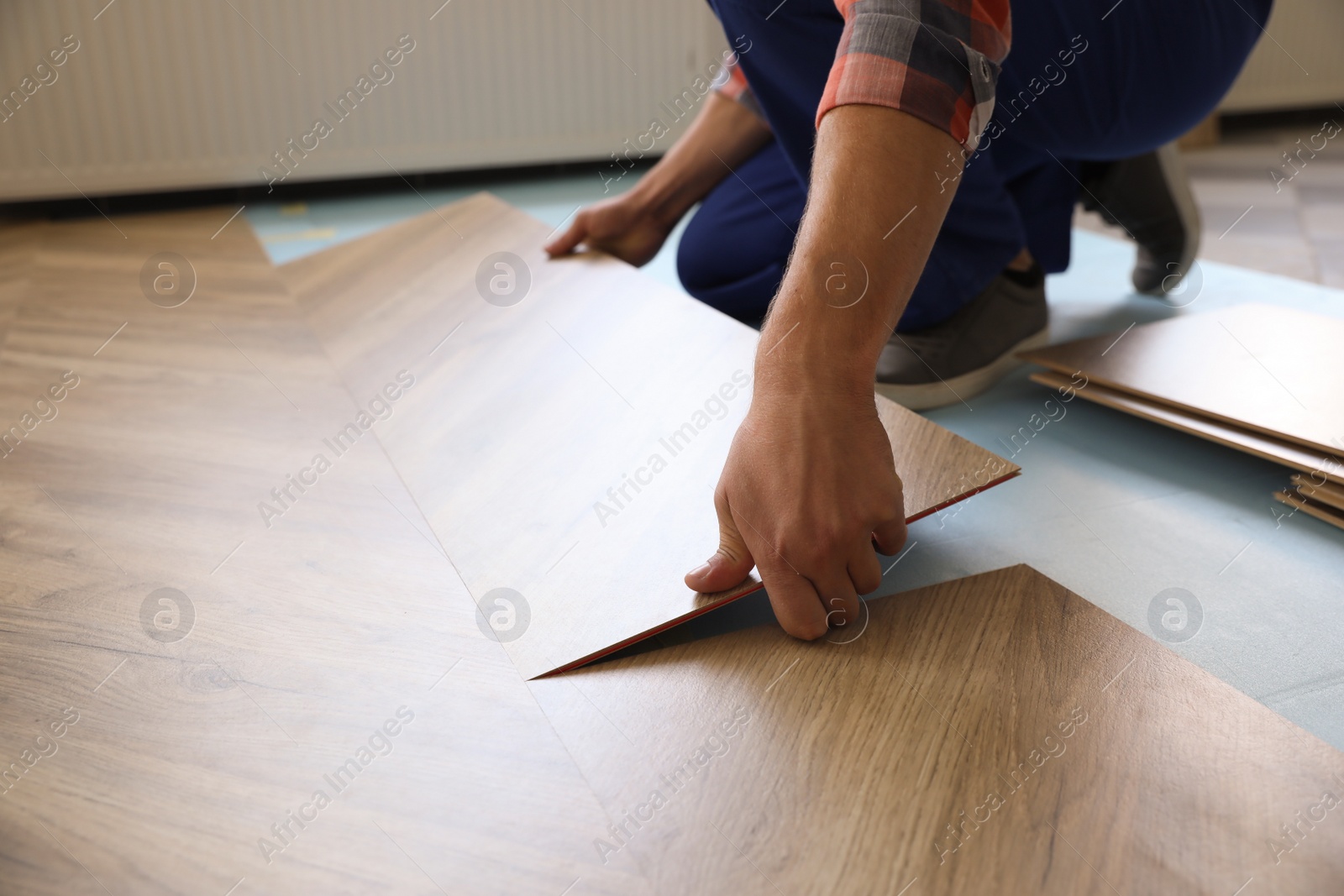 Photo of Worker installing laminated wooden floor indoors, closeup