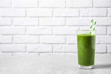 Photo of Delicious fresh green juice with straws on grey table against brick wall, space for text