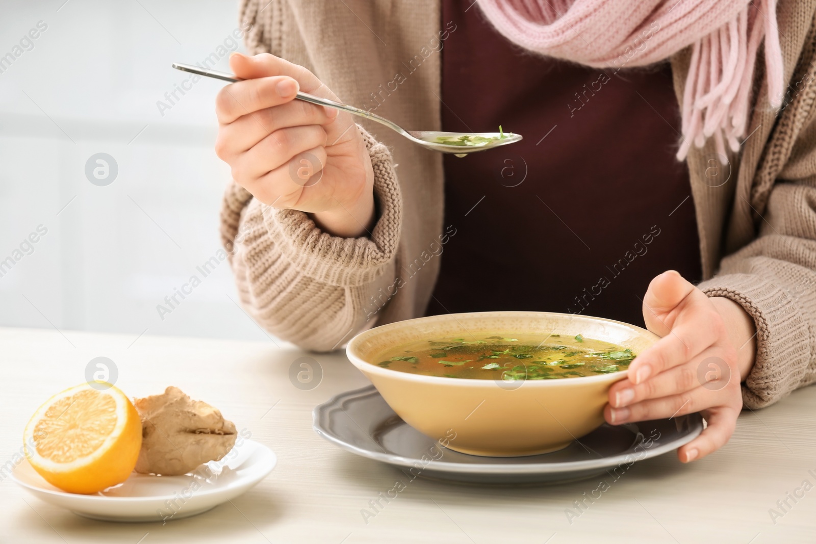 Photo of Sick young woman eating broth to cure cold at table in kitchen