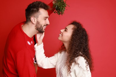Photo of Lovely couple under mistletoe bunch on red background