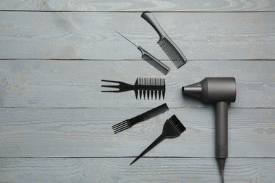 Hair dryer and professional hairdresser tools on wooden table, flat lay