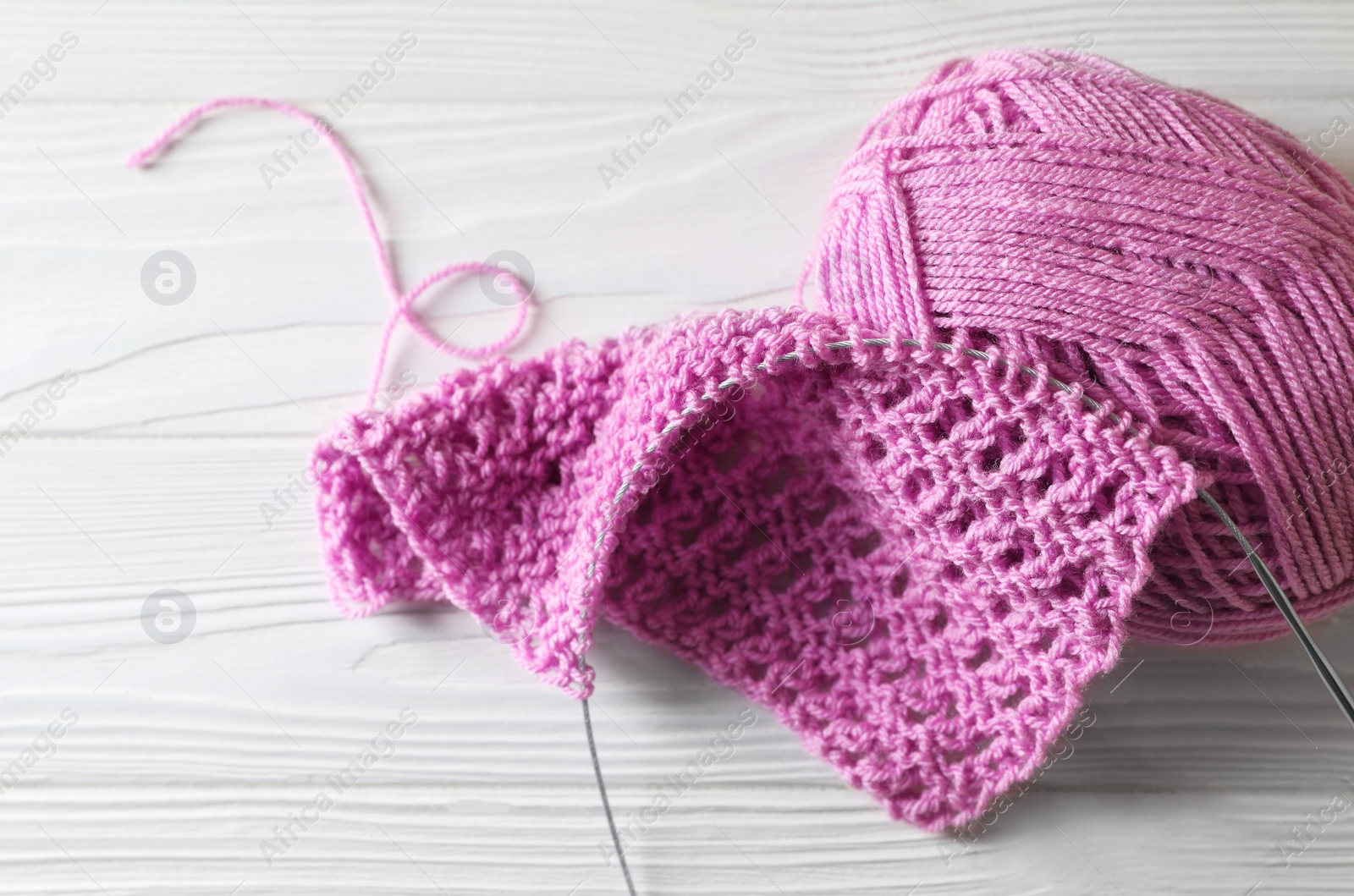 Photo of Soft pink yarn, knitting and metal needle on white wooden table, closeup