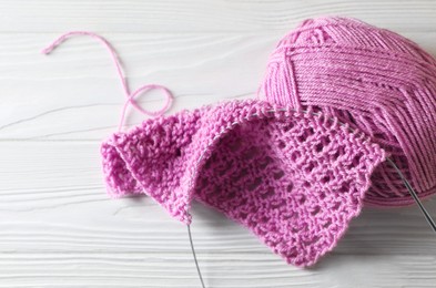 Photo of Soft pink yarn, knitting and metal needle on white wooden table, closeup