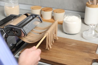 Photo of Woman making soba with pasta machine at table in kitchen, closeup