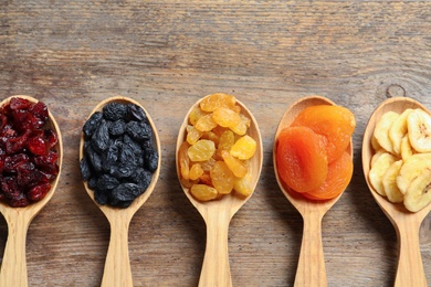 Photo of Spoons of different dried fruits on wooden background, top view with space for text. Healthy lifestyle