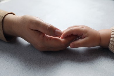 Woman holding hands with her little daughter at light grey table, closeup