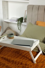 White tray with modern laptop and cup of aromatic tea on bed indoors