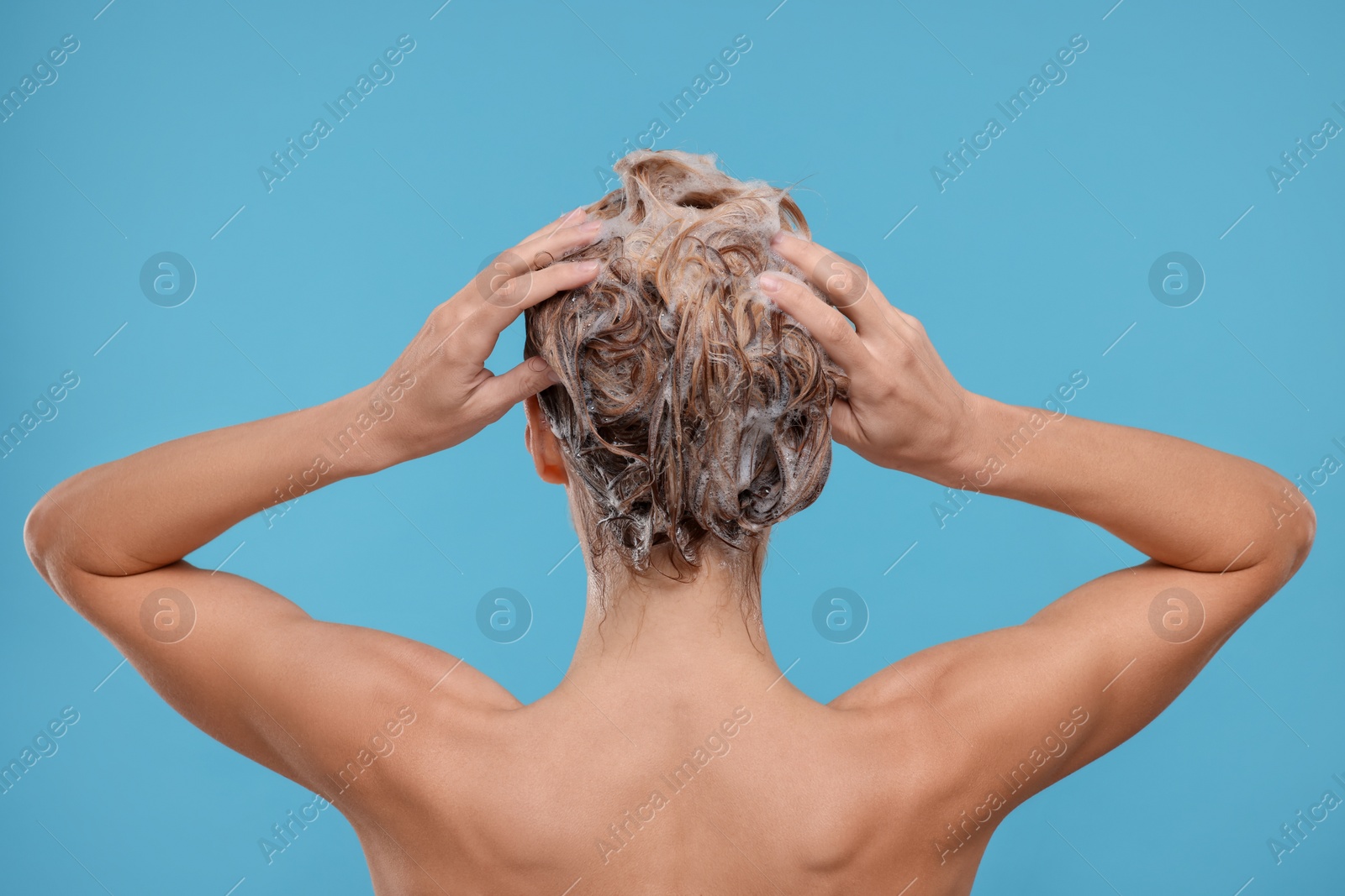 Photo of Woman washing hair on light blue background, back view