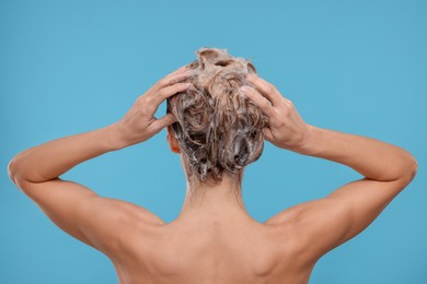 Photo of Woman washing hair on light blue background, back view