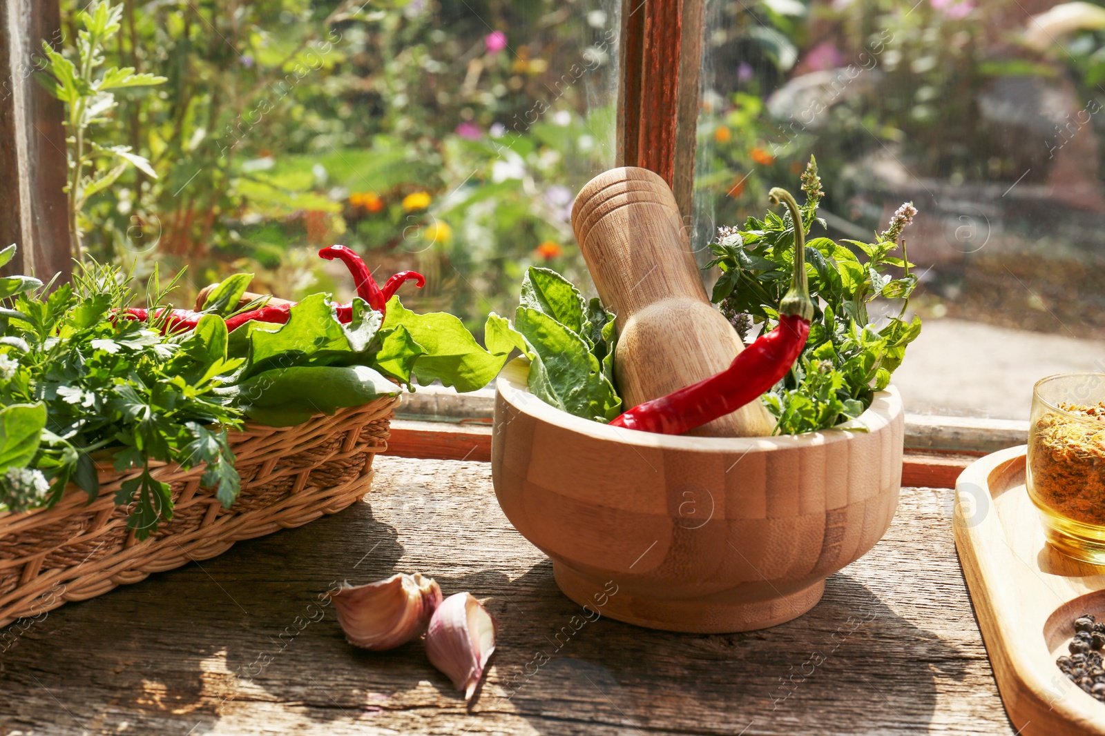 Photo of Mortar with pestle, fresh green herbs and different spices on wooden table near window