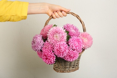 Woman with bouquet of beautiful asters on light background, closeup. Autumn flowers