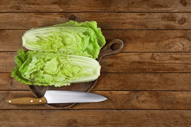 Photo of Halves of fresh ripe Chinese cabbage and knife on wooden table, flat lay. Space for text