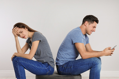 Man with smartphone ignoring his girlfriend on light background. Relationship problems