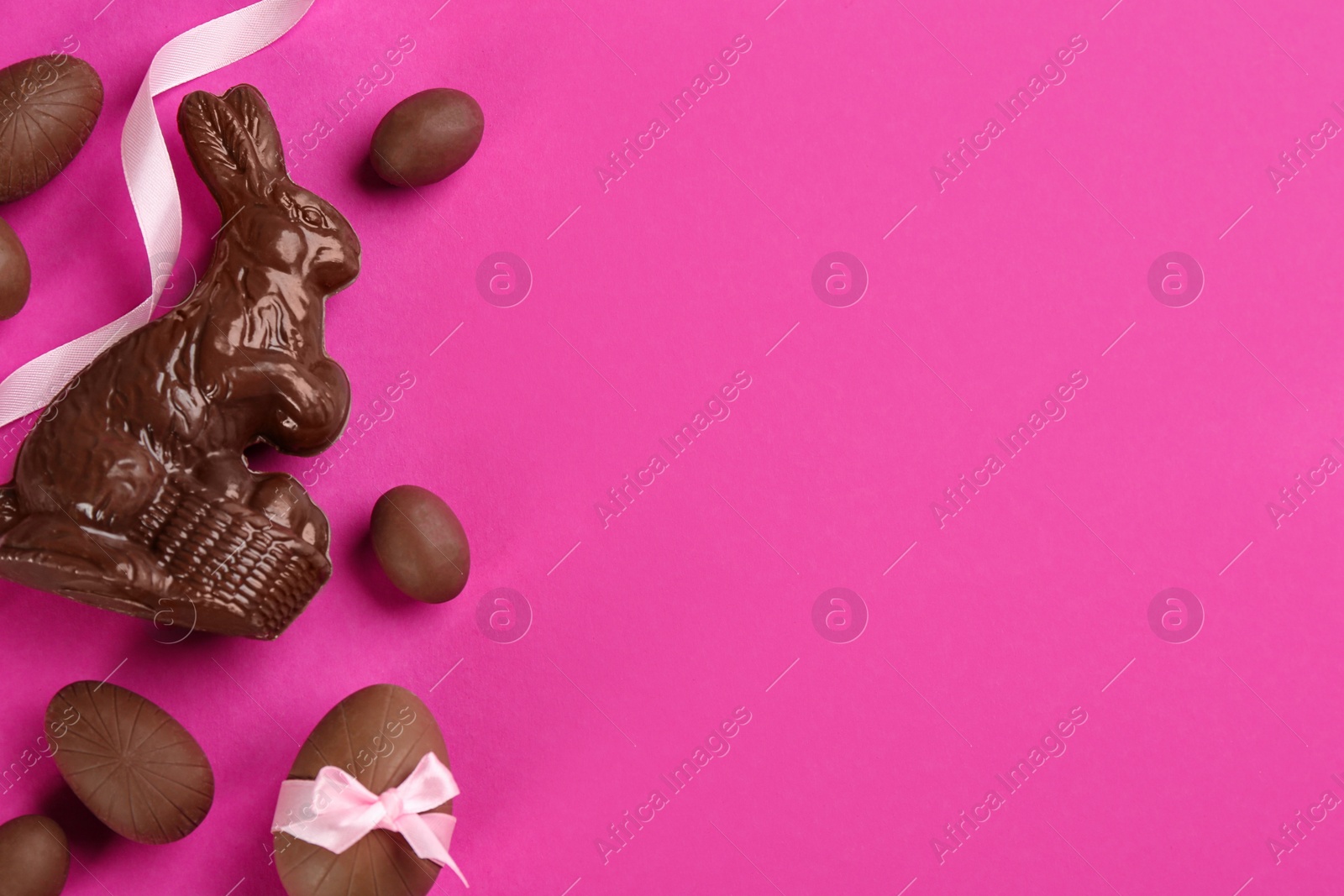 Photo of Flat lay composition with chocolate Easter bunny and eggs on pink background. Space for text