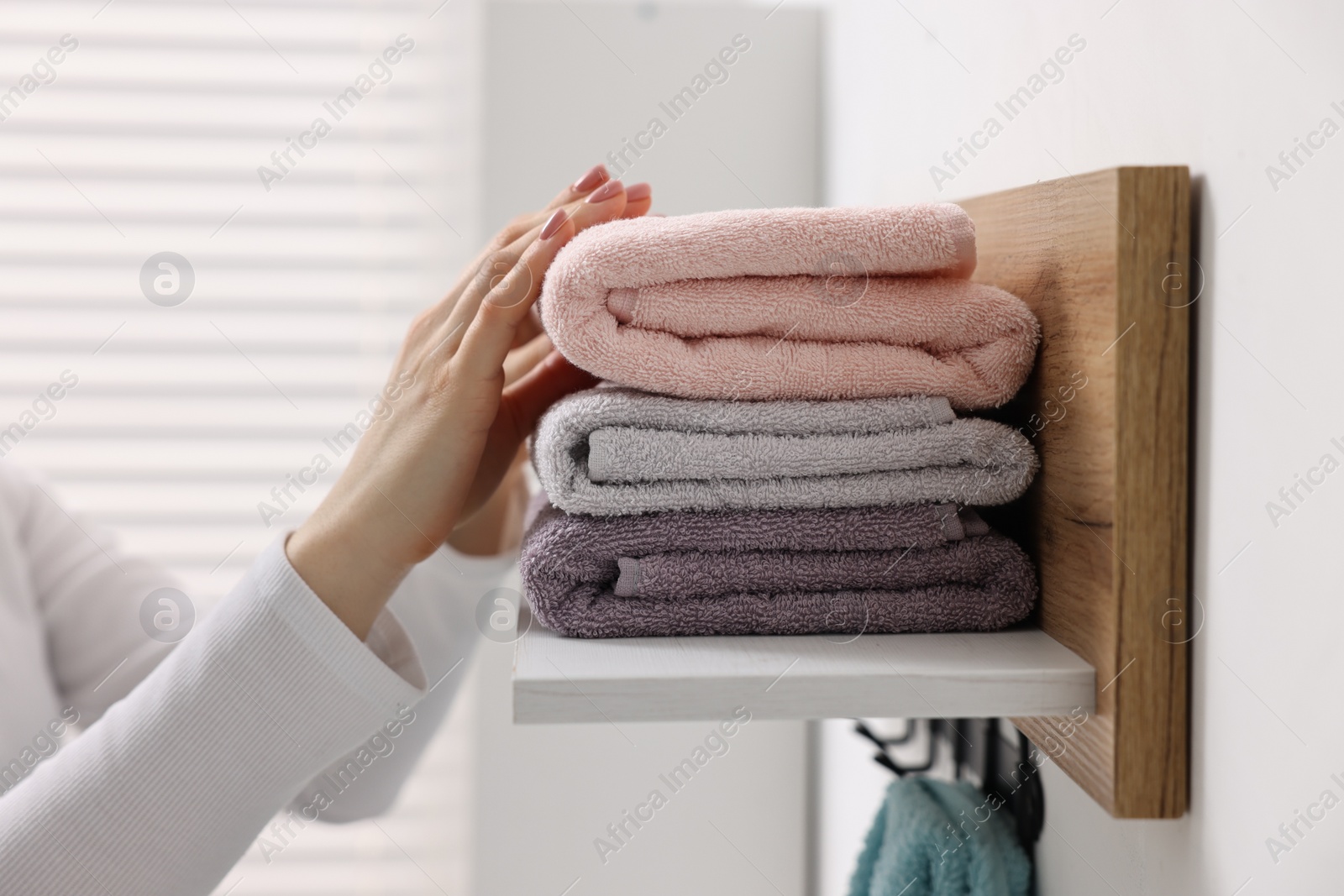 Photo of Woman stacking clean towels on shelf indoors, closeup