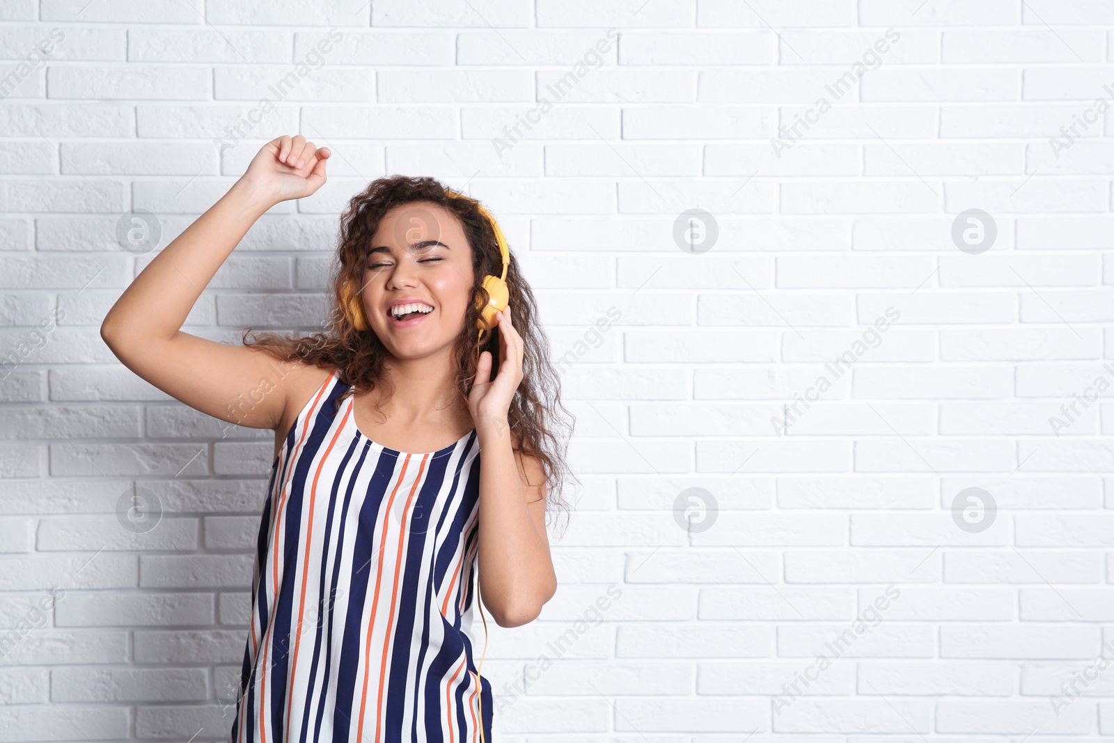 Photo of African-American woman listening to music with headphones near brick wall, space for text