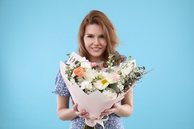 Happy woman with bouquet of beautiful flowers on light blue background