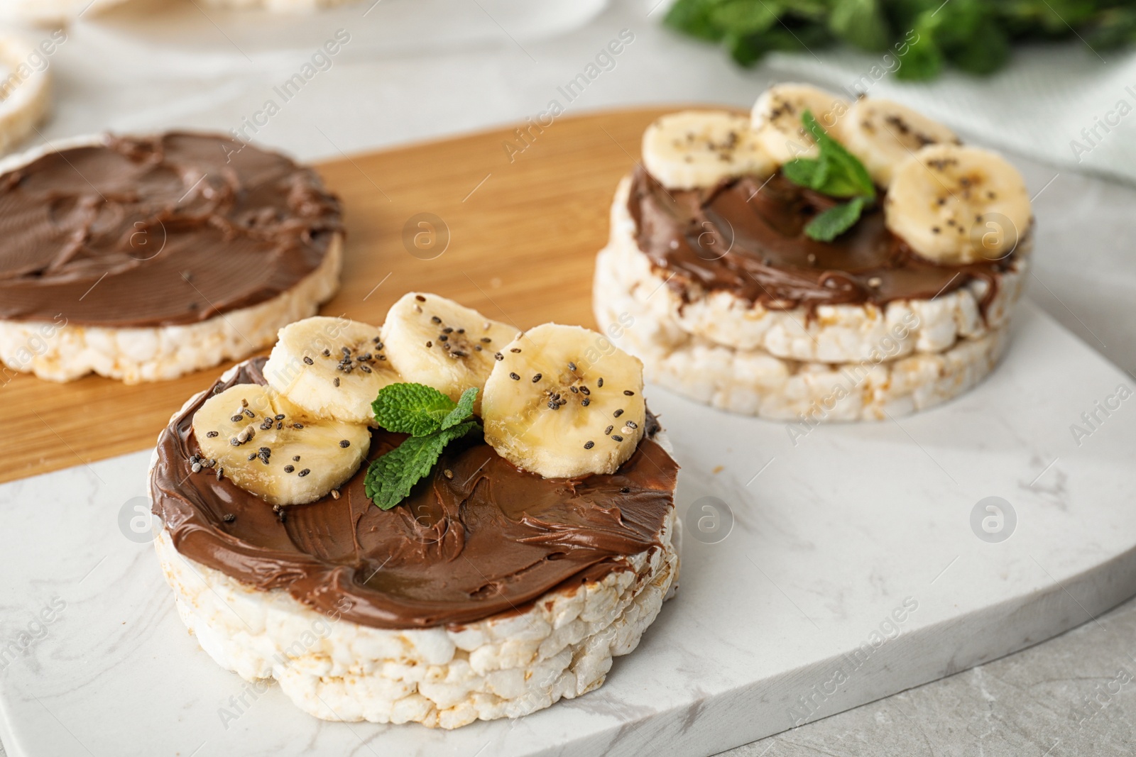 Photo of Puffed rice cakes with chocolate spread, banana and mint on board, closeup