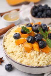 Photo of Bowl of tasty couscous with blueberries, pumpkin and mint on table, closeup