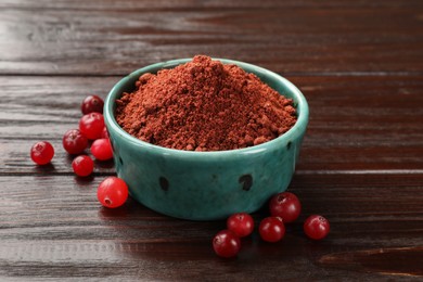 Photo of Dried cranberry powder in bowl and fresh berries on wooden table