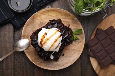 Photo of Tasty brownies served with ice cream and caramel sauce on wooden table, flat lay