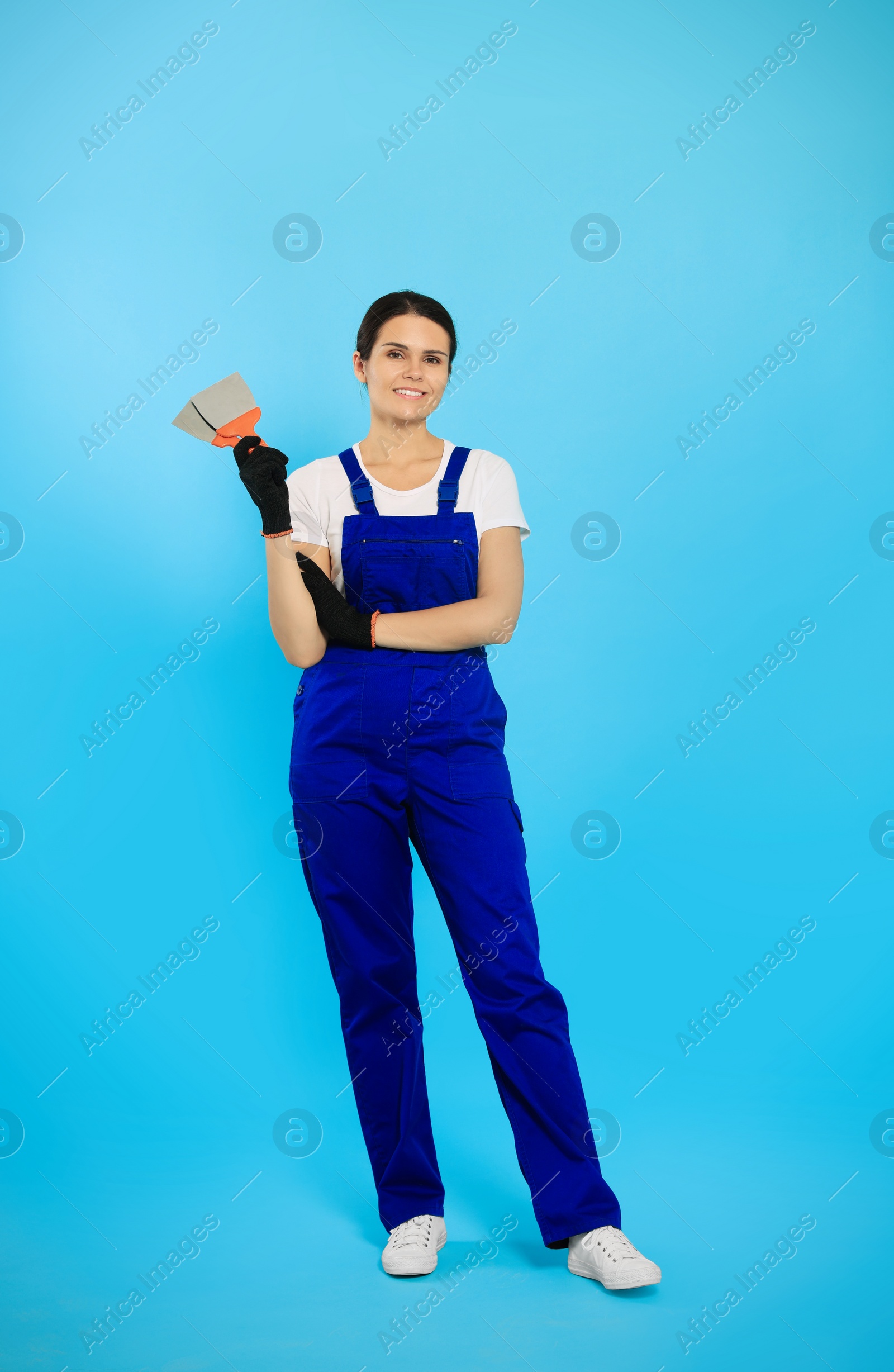 Photo of Professional worker with putty knife on light blue background
