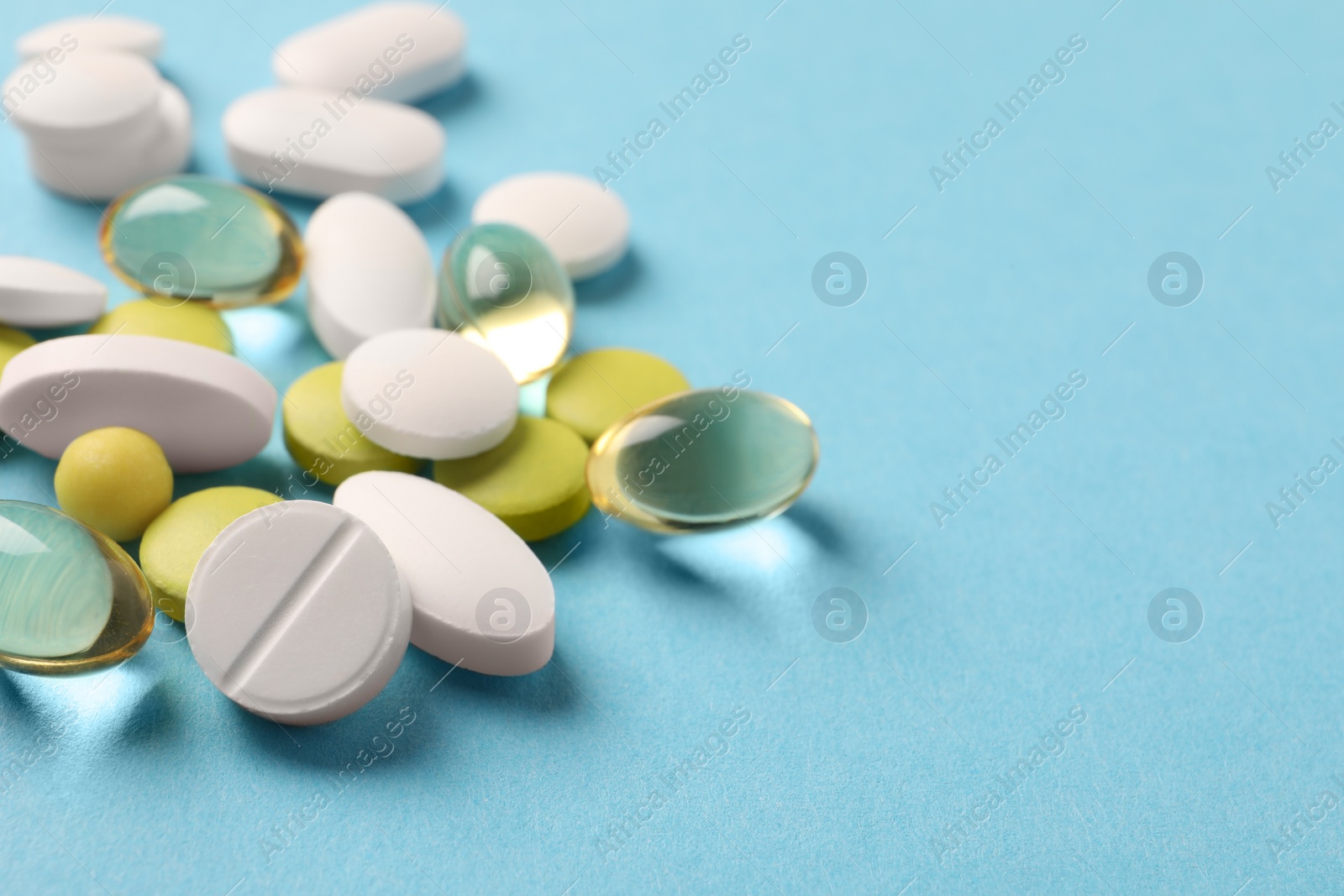 Photo of Pile of different pills on light blue background, closeup. Space for text