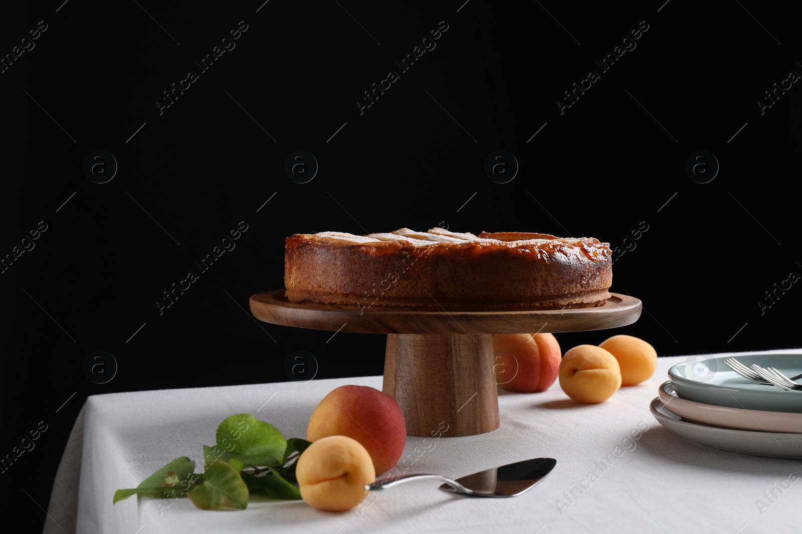 Photo of Tasty apricot pie with powdered sugar on table against black background