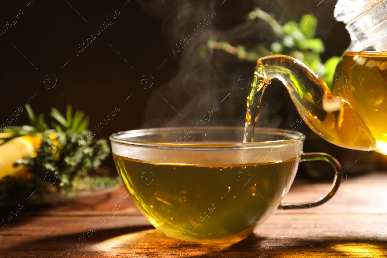 Photo of Pouring aromatic herbal tea into cup on wooden table, closeup