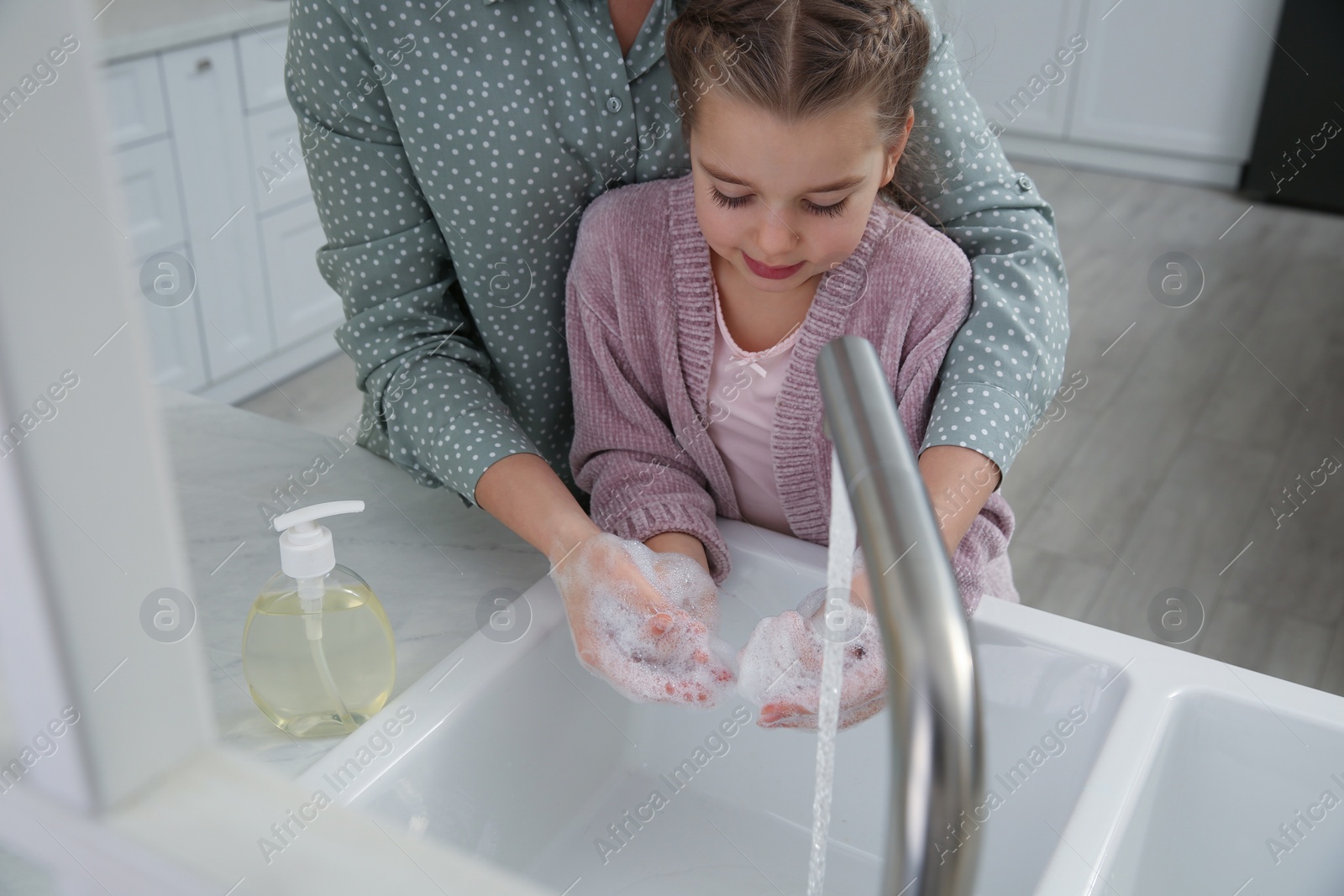 Photo of Mother and daughter washing hands with liquid soap together in kitchen, closeup