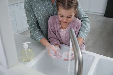 Photo of Mother and daughter washing hands with liquid soap together in kitchen, closeup