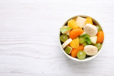 Photo of Delicious fresh fruit salad in bowl on white wooden table, top view. Space for text