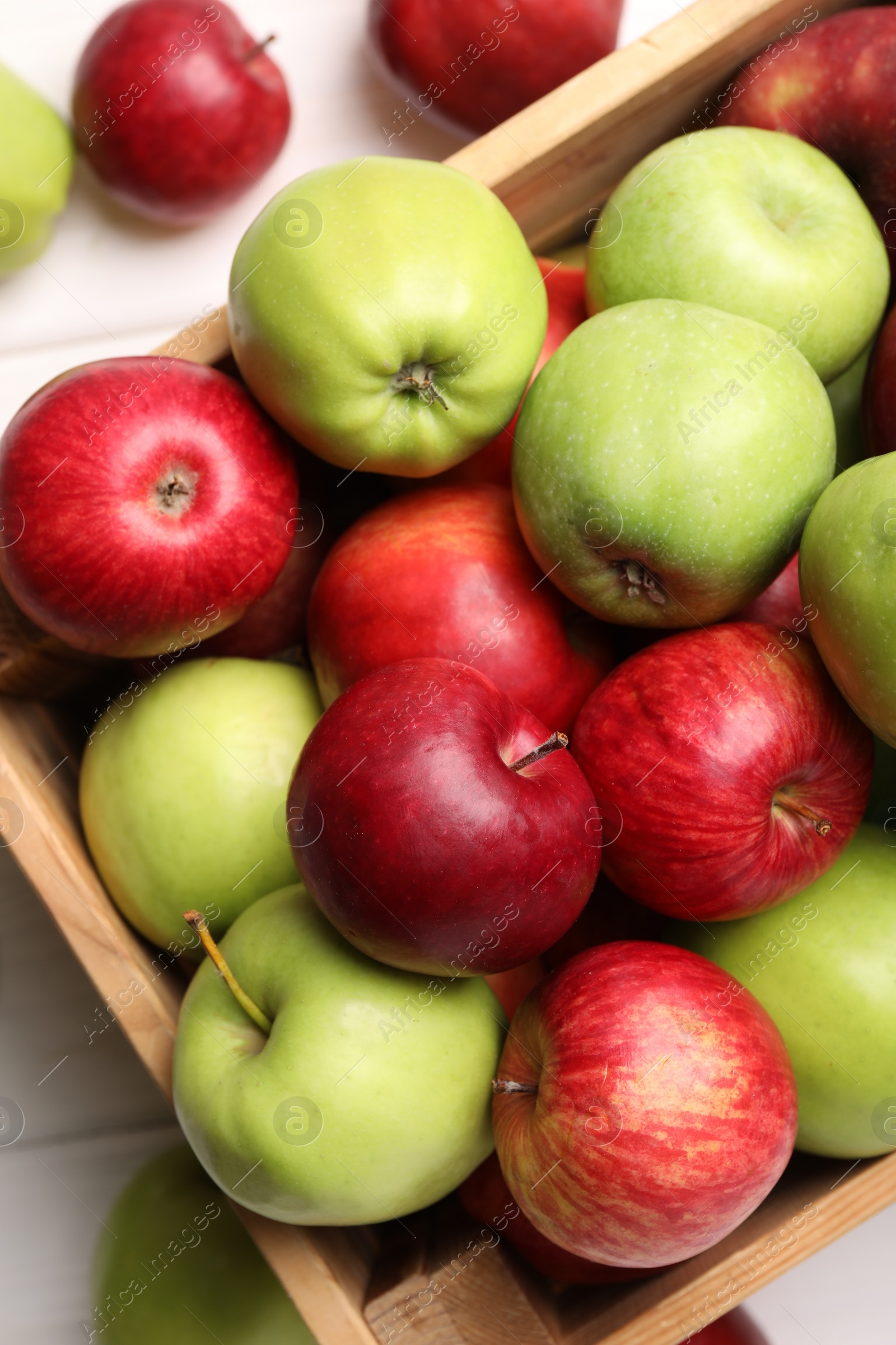 Photo of Wooden crate with ripe red and green apples on white table, flat lay