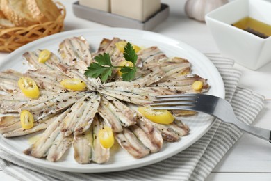 Photo of Tasty pickled anchovies with spices and fork on white wooden table, closeup