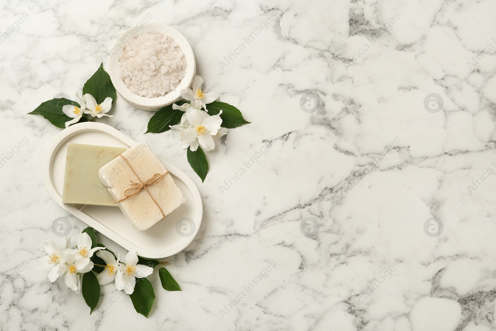 Photo of Beautiful jasmine flowers, sea salt and soap bars on white marble table, flat lay. Space for text