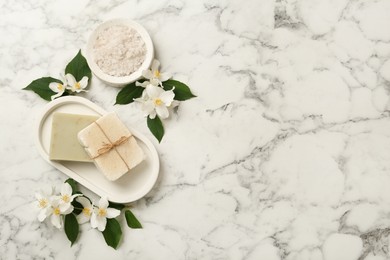 Beautiful jasmine flowers, sea salt and soap bars on white marble table, flat lay. Space for text