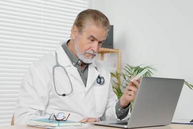 Photo of Senior doctor with laptop consulting patient at wooden desk in clinic. Online medicine