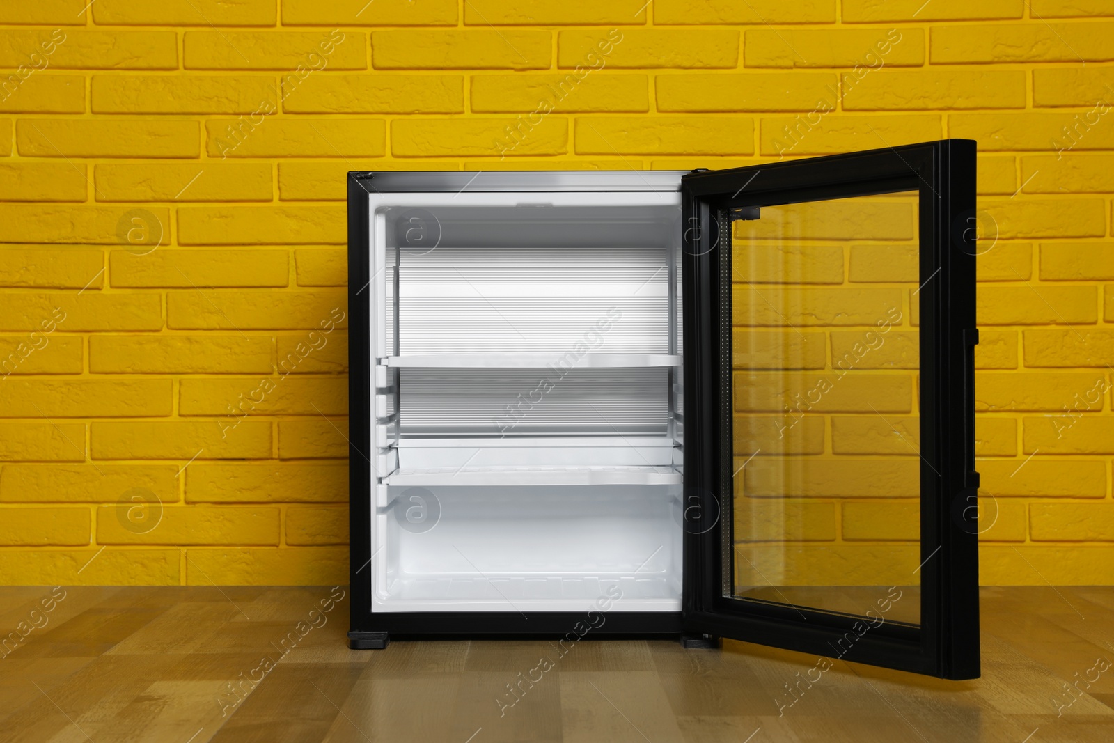 Photo of Empty mini bar with open glass door near yellow brick wall