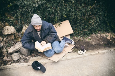 Poor homeless man with book on street in city