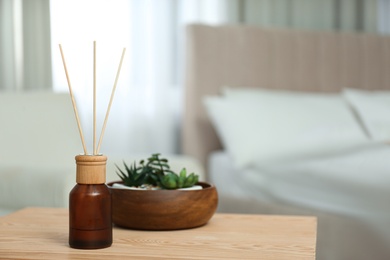 Photo of Air reed freshener and houseplants on wooden table in bedroom. Space for text