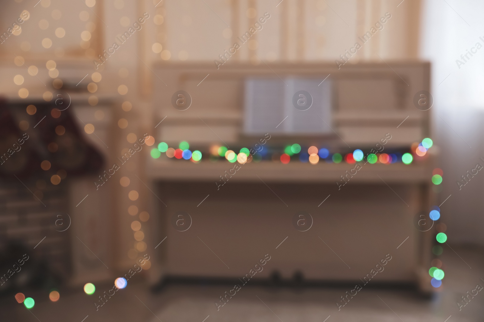 Photo of Blurred view of white piano with fairy lights indoors. Christmas music