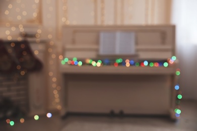 Photo of Blurred view of white piano with fairy lights indoors. Christmas music