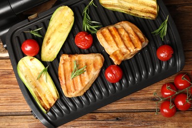 Photo of Electric grill with tasty meat, rosemary and vegetables on wooden table, flat lay