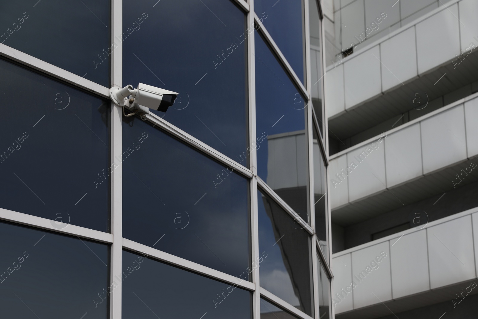 Photo of Modern building with tinted windows and CCTV camera, low angle view. Urban architecture