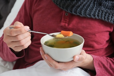 Photo of Sick young man eating broth to cure cold in bed at home