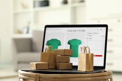 Photo of Online store. Laptop, small shopping bags and mini parcels on table indoors